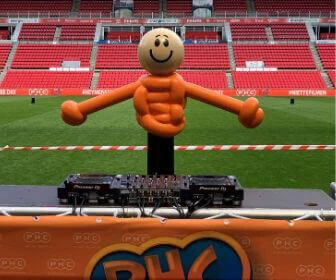 Op het veld in het Phillips stadion staat een paal met een lachend gezichtje er op waaraan twee armen zijn toegevoegd. Deze paal staat achter een DJ tafel en moet de DJ voorstellen.