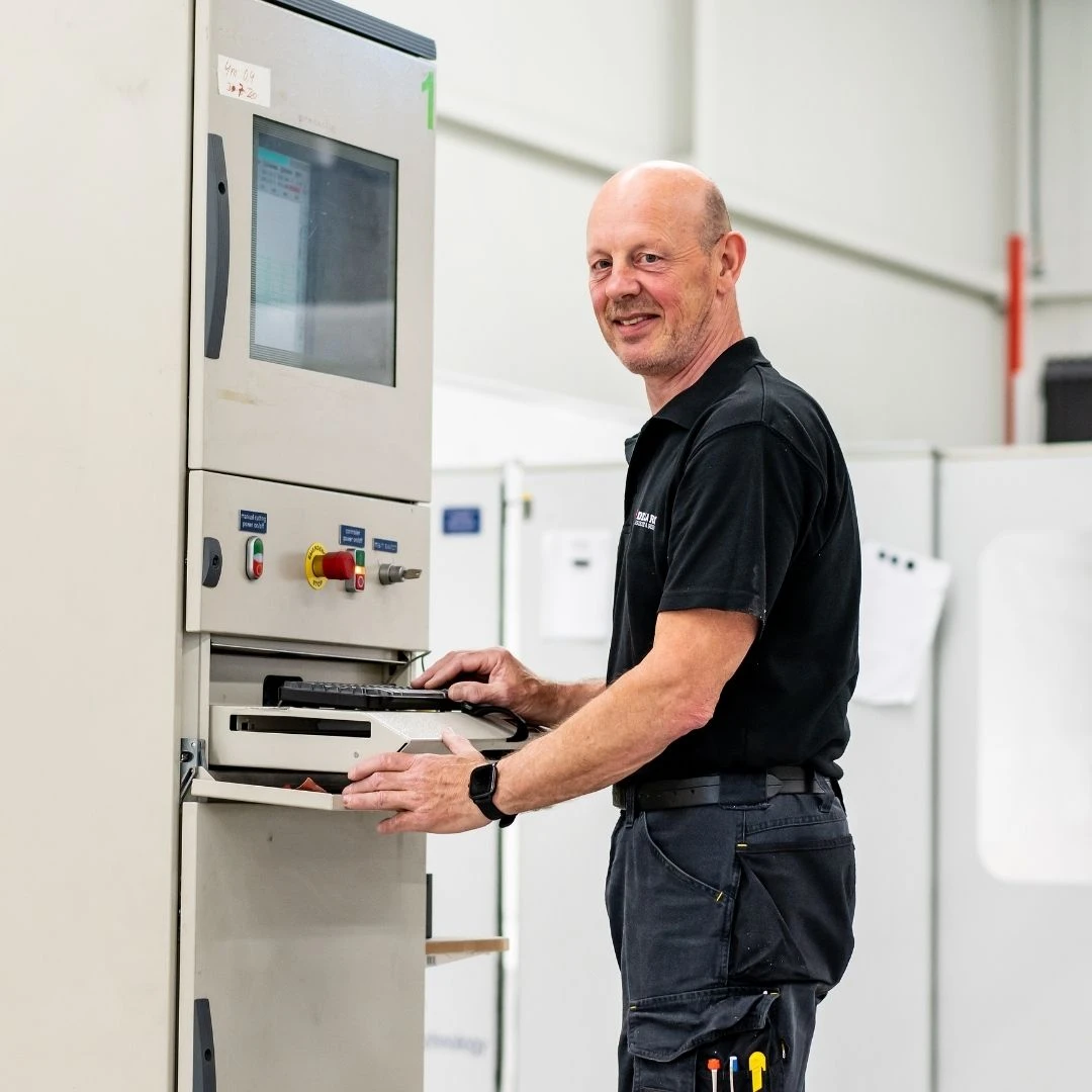 Hans Klaassens staat achter het bedieningspaneel van onze freesmachine. Hij draagt onze werkkleding.