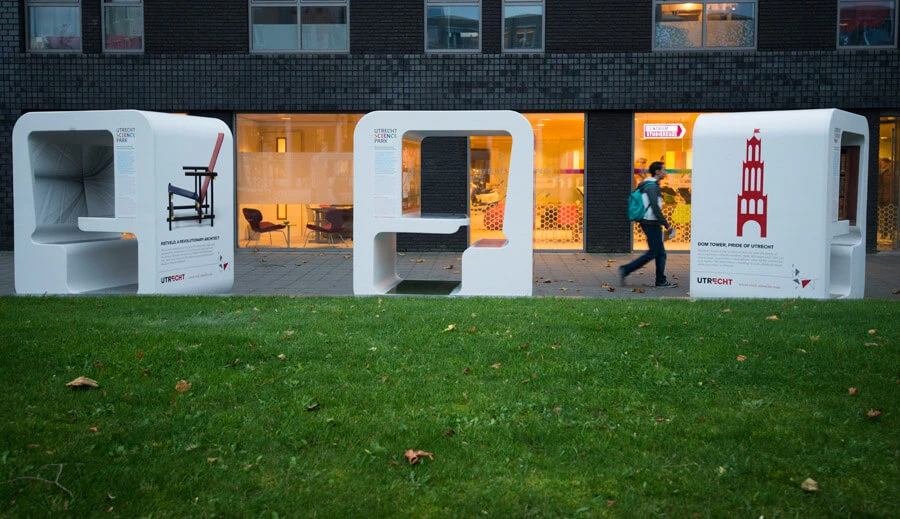 Iemand met een groene rugzak loopt langs drie witte science cubes die uit piepschuim zijn gemaakt.