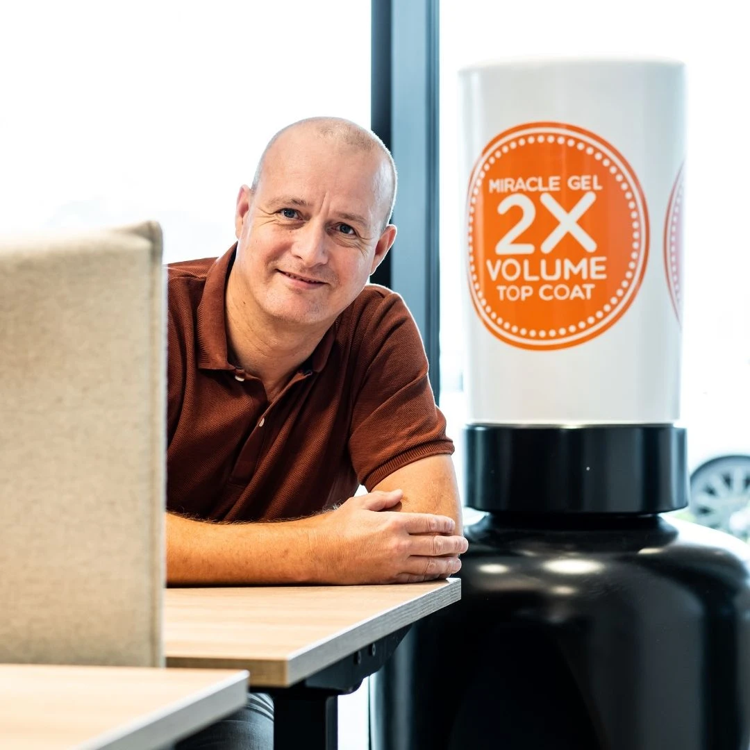 Serge Geertsema draagt een bruine polo en leunt op zijn bureau dat naast een blow up van tempex staat.