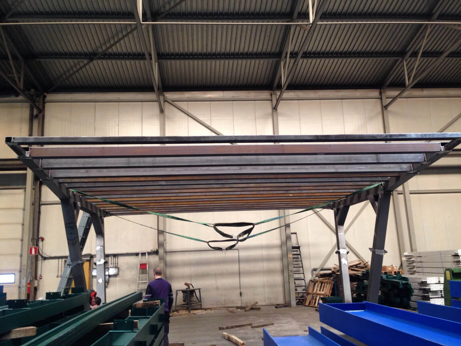 Binnen onze werkplaats staat een ijzeren constructie waaraan groene spanbanden hangen.